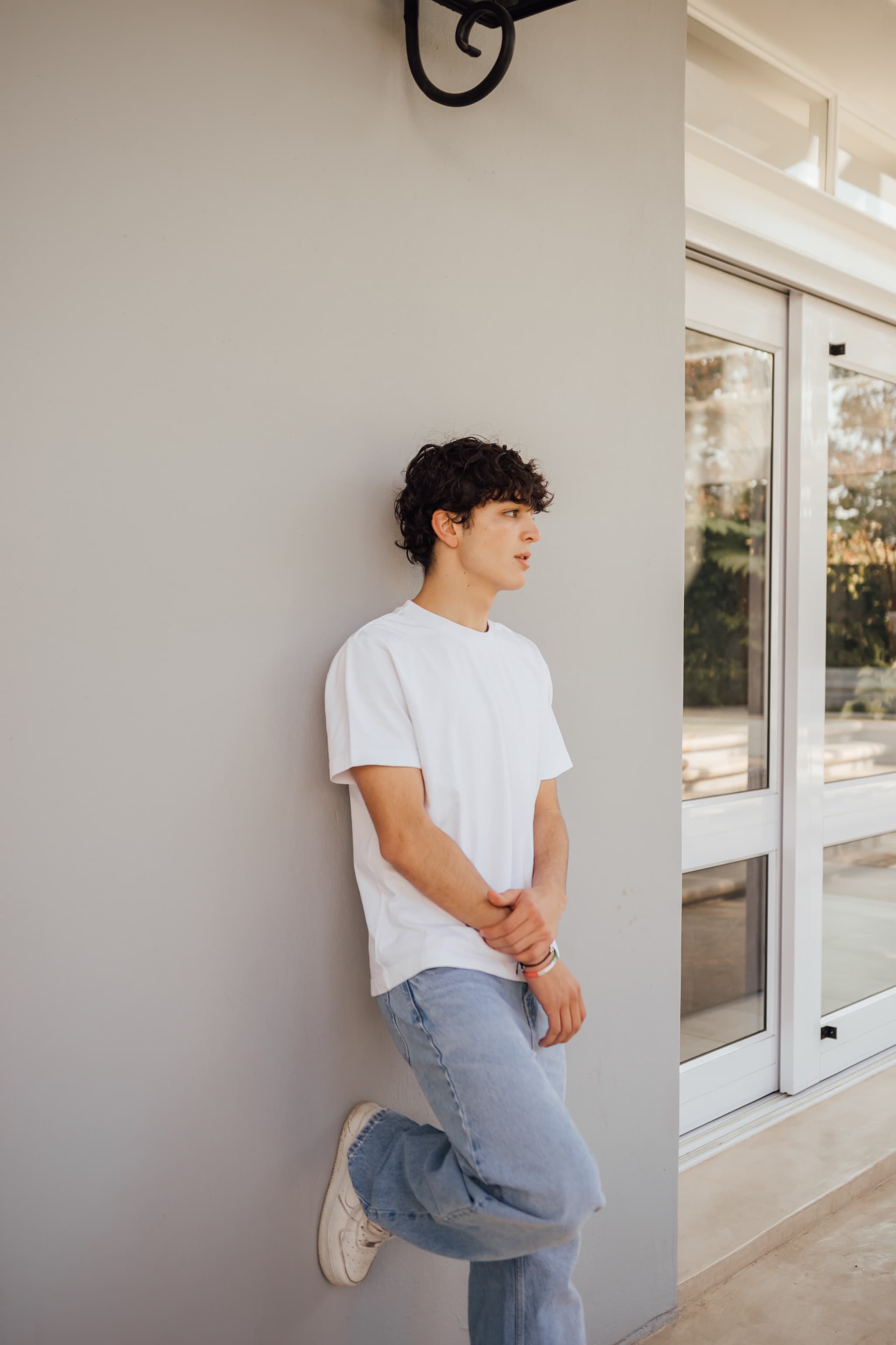 A model in a white tee and light wash jeans, leaning against a grey wall