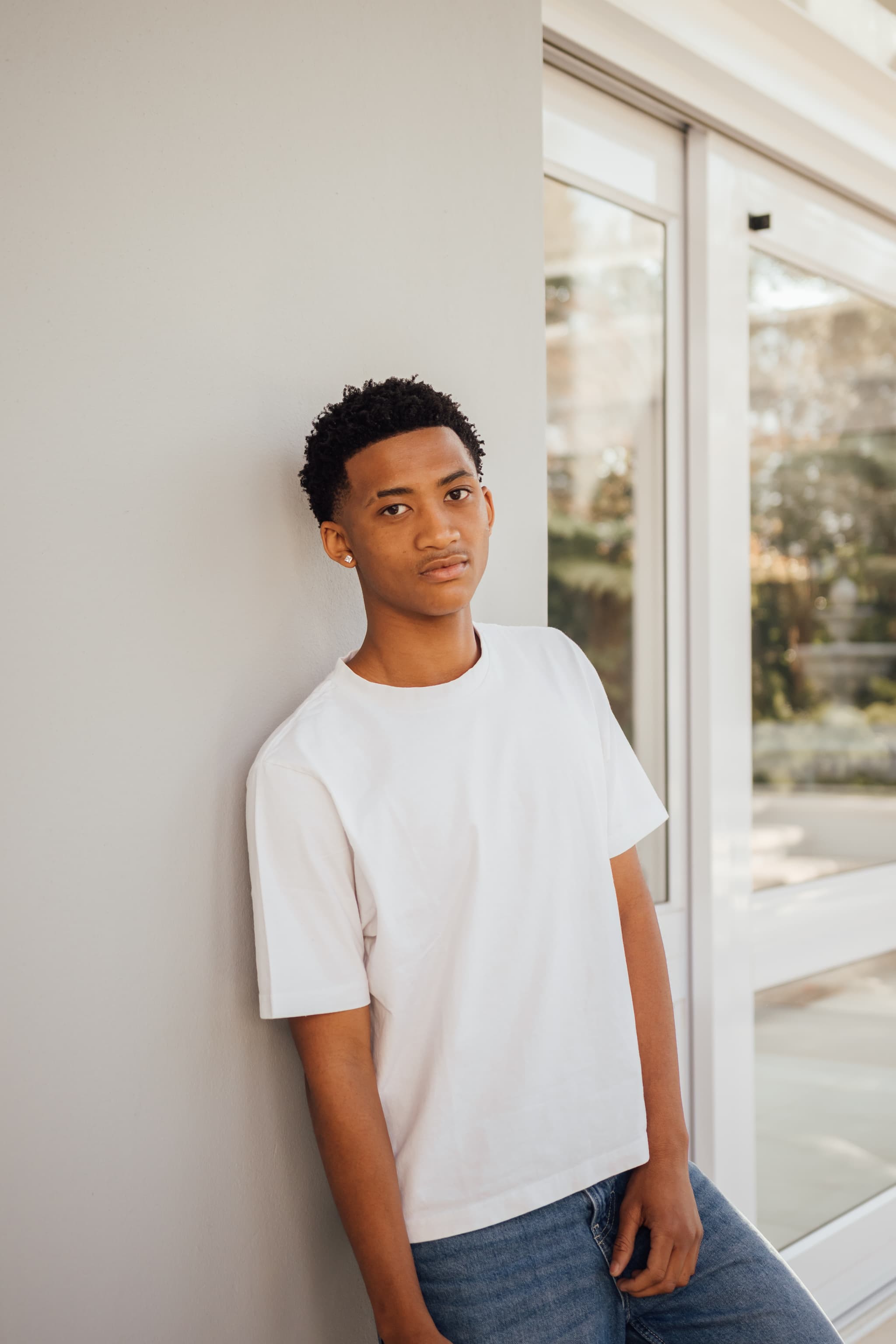 Musa leaning against a grey wall beside glass doors