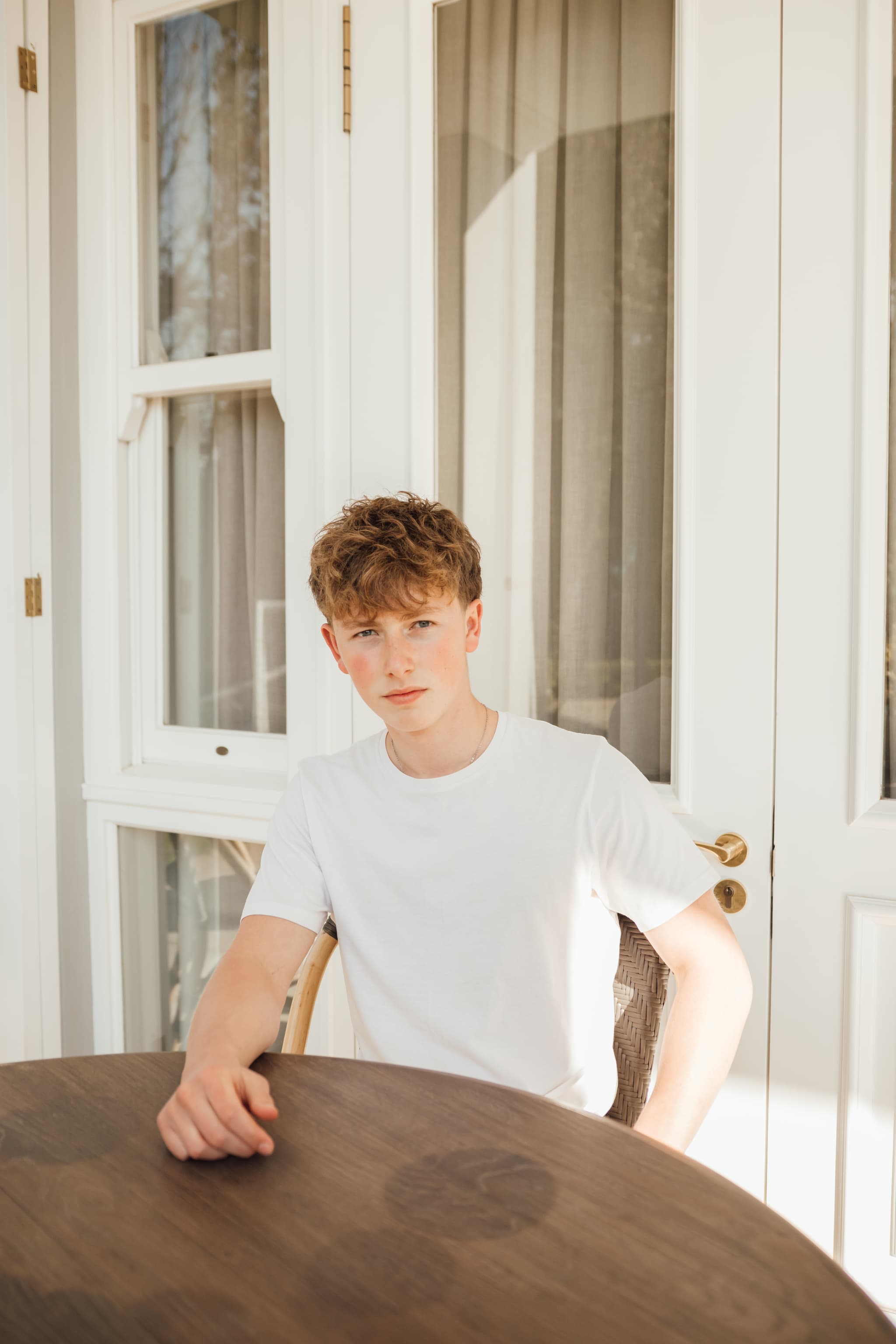 Sean at a wooden table on a sunlit porch, in a white tee