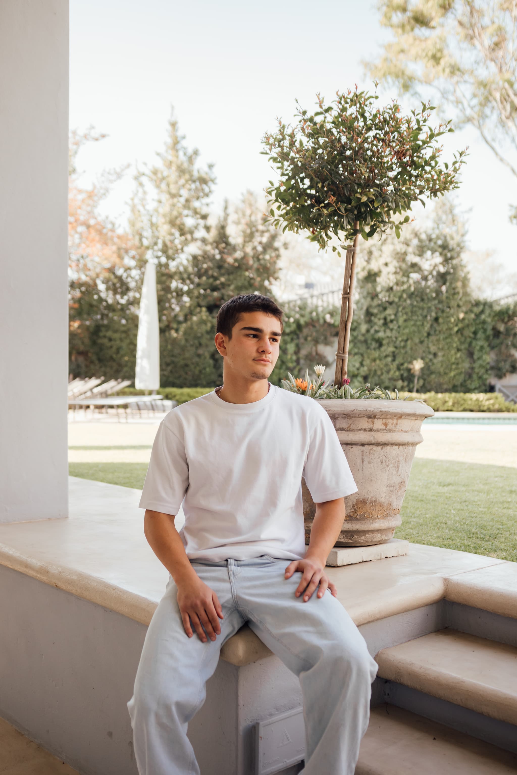 Lorenzo seated on a garden ledge beside a potted tree